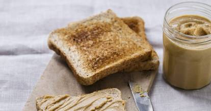 Toast mit Erdnussbutter bestrichen auf einemHolzbrett mit angelegtem Messer 